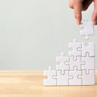 Hand arranging jigsaw puzzle stacking as step stair on wooden table. Business concept for growth success process