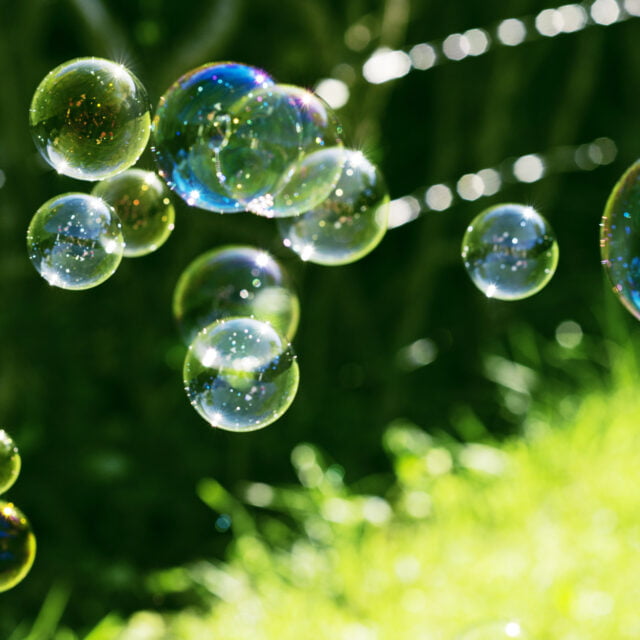 Soap bubbles fly through the air next to field of grass